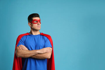 Wall Mural - Man wearing superhero cape and mask on light blue background. Space for text