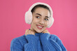 Beautiful young woman wearing earmuffs on pink background