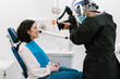 © Ezequiel Giménez/Stocksy - Dentist with mask and protective clothing, taking a photo of his patient.
