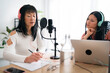 © Studio Marmellata/Stocksy - Asian female podcasters checking script before recording session