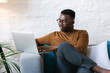 © Mihajlo Ckovric/Stocksy - Young businessman sitting at the couch in the office using his laptop