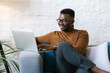 © Mihajlo Ckovric/Stocksy - Young businessman sitting at the couch in the office using his laptop