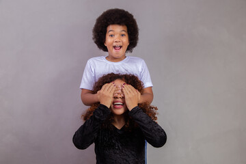 Wall Mural - African American boy holding his mother closed eyes. grey background. Mothers Day. Brazilian family.