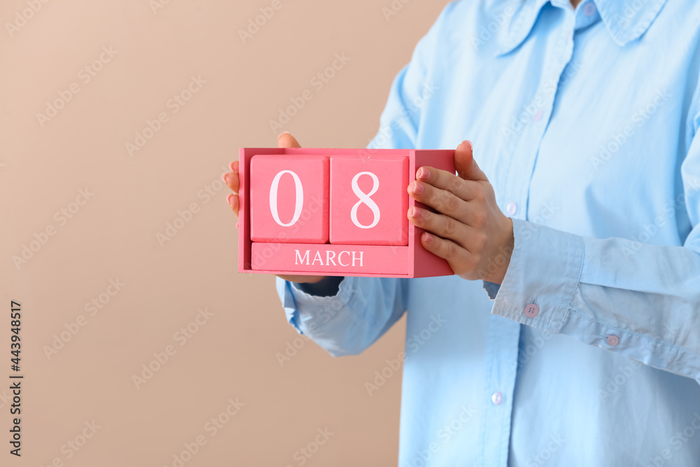 Woman holding cube calendar with date MARCH 8 on color background