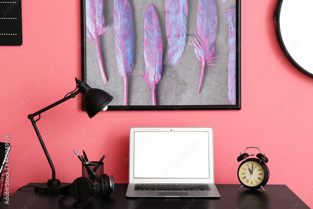 Modern workplace with laptop and headphones near color wall