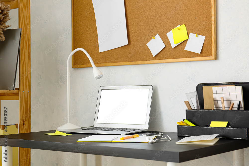 Modern workplace with laptop near light wall
