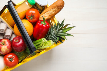 Shopping basket with food on white wooden background