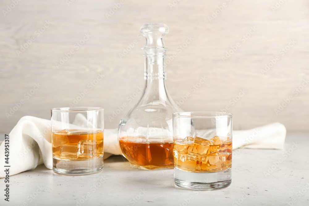 Jug and glasses of cold whiskey on light background