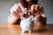 © Farknot Architect - Closeup image of a woman putting coins into piggy bank for saving money concept