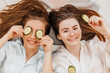 © Daria Lukoiko - Two girls make homemade face and hair beauty masks. Cucumbers for the freshness of the skin around the eyes. Women take care of youthful skin. Girlfriends laugh at home lying on the floor on pillows.