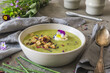 Creamy herbes soup with sorrel, edible blooms and croutons as topping. Gray concrete background.