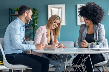 Happy young couple signing bank loan agreement with real-estate agent to buying the house in the office.