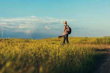 Wall Mural - Young handsome man, in a cap and glasses, with a backpack, traveling and walking in nature, a man with a bouquet of wildflowers