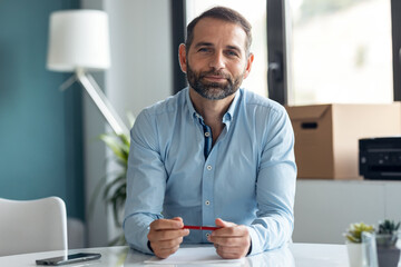 Confident mature man explaing something looking at camera while doing video call in the office at home.