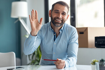 Confident mature man explaing something looking at camera while doing video call in the office at home.