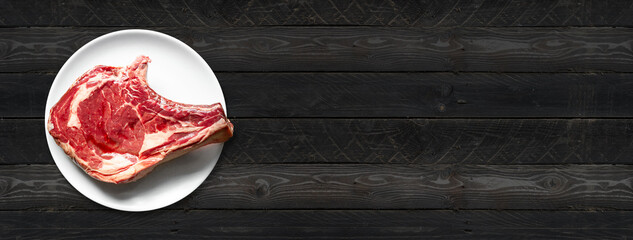 Wall Mural - Beef prime rib and plate isolated on black wooden background. Horizontal banner