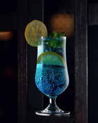 Alcoholic drink. Exotic blue lagoon cocktail with mint leaf, lemon slice and air bubbles on black background. Soft focus. Copy space.