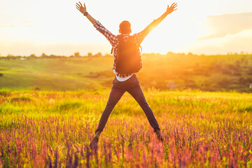 Wall Mural - Traveler with raised hands standing on a hill in green grass and enjoying a majestic sunset, Successful man enjoying triumph