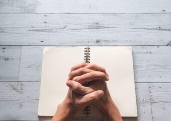 Praying hands on book blank page and sunlight nature shadow on white wooden texture background top view,Pray god concept