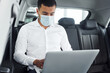 © standret - Works by using laptop. Young man in white shirt is sitting inside of a modern new automobile