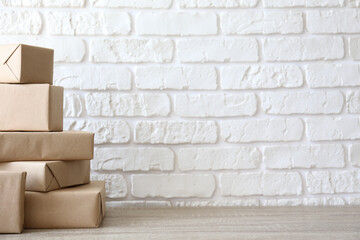 Stacked packages of different sizes wrapped in craft paper prepared for shipping out. Bunch of parcel boxes on the table. Close up, copy space for text, white brick wall background.