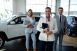 Salesteam in dealership, three beautiful consultants or managers in elegant suit looking at camera.