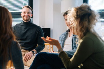 Wall Mural - Close-up of confident male trainer leads corporate training with creative business team sitting in circle on background of window. Businessman talking during team-building seminar in modern office.