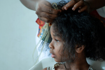 Close up African hairstylist braided hair of afro little girl, mother spend time with girl child take care and relaxing at home together, selective focus