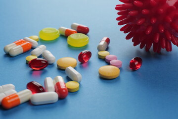 Multicolored medical pills of various shapes and imitation of a coronavirus cell on a blue background