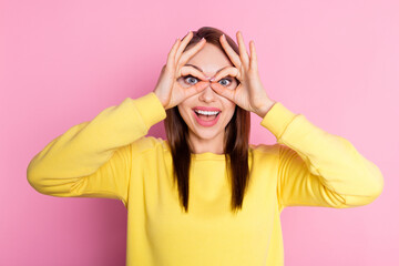 Wall Mural - Photo portrait girl smiling keeping fingers like binocular playful isolated pastel pink color background