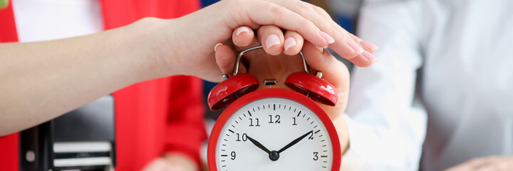 Two business women turning off alarm clock at workplace closeup