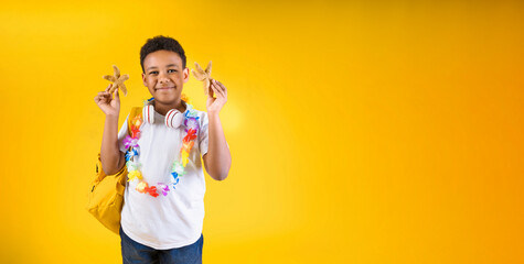 Happy boy holding sea stars wearing hawaiian lei flower necklace with backpack on yellow background