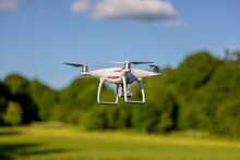 Unmanned Aerial Vehicle Against A Blue Sky And Green Trees - A Drone In The Air
