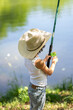 A boy in a straw hat is spinning a reel with a line on a fishing rod. Child fishing on a summer day.