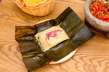 Mexican Tamale Of Cochinita Pibil Stewed Inside Corn Cob Leaf With Volcanic Stone Molcajete Filled With Pico De Gallo