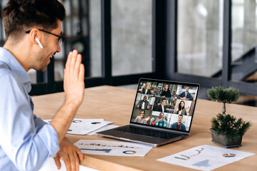 Wall Mural - Distant communication. Caucasian man having virtual business meeting, talking with successful multi ethnic people via video call, using laptop, sits in office, planning marketing strategy and ideas