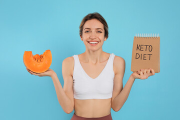 Woman holding notebook with phrase Keto Diet and pumpkin on light blue background