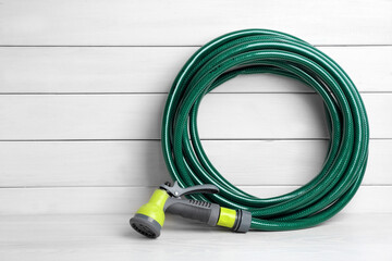 Wall Mural - Green garden hose with spray gun on white wooden table, space for text