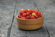 A Wooden Bowl Filled With Wild Strawberries On A Wooden Table.