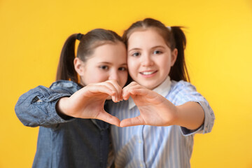 Poster - Cute twin girls making heart shape with their hands on color background