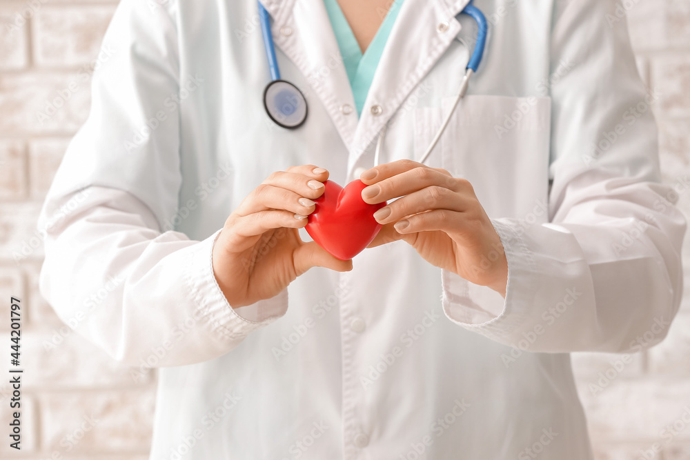 Female cardiologist with red heart near brick wall, closeup