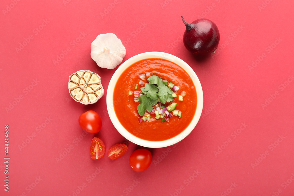 Bowl with tasty gazpacho and vegetables on color background