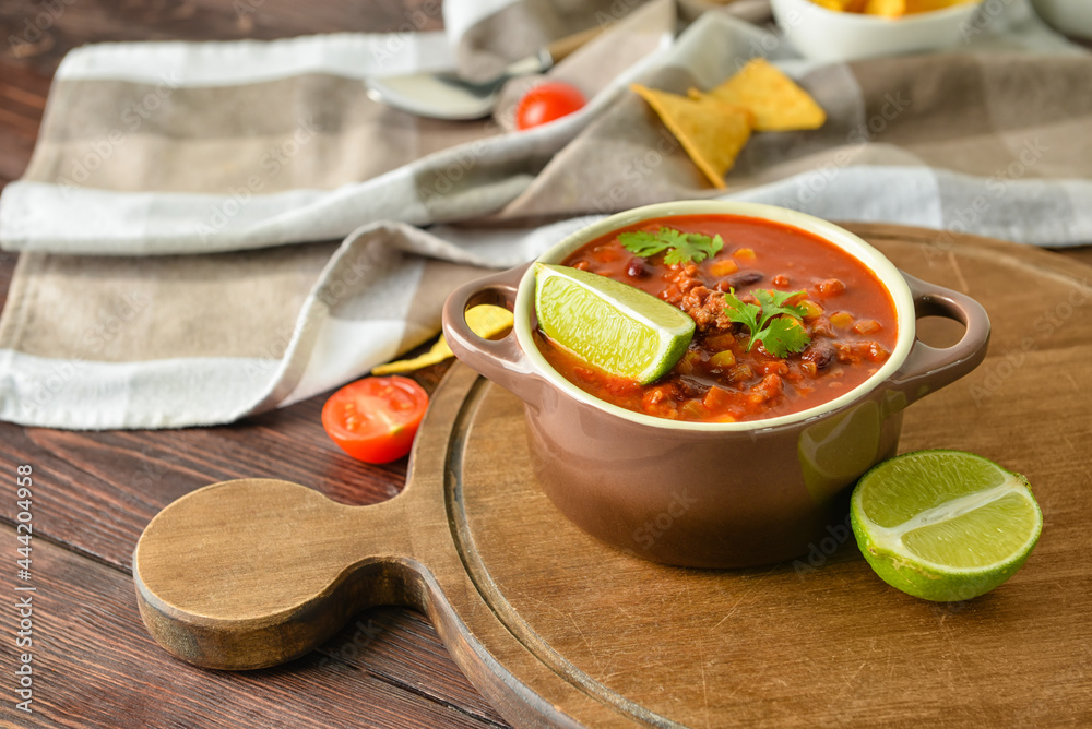 Pot with delicious chili con carne on wooden background