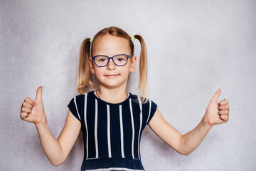 Wall Mural - Little girl wearing eyeglasses with her thumbs up, children's Pediatric Ophthalmology, common eye problems in children