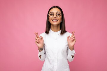 Photo of young positive happy smiling beautiful woman with sincere emotions wearing stylish clothes isolated over background with copy space and holding fingers srossed for good luck