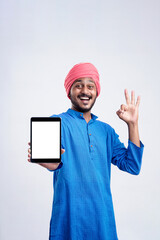 Wall Mural - Young indian man in traditional wear and showing tablet over white background.