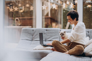 Young woman with cat working on laptop from home