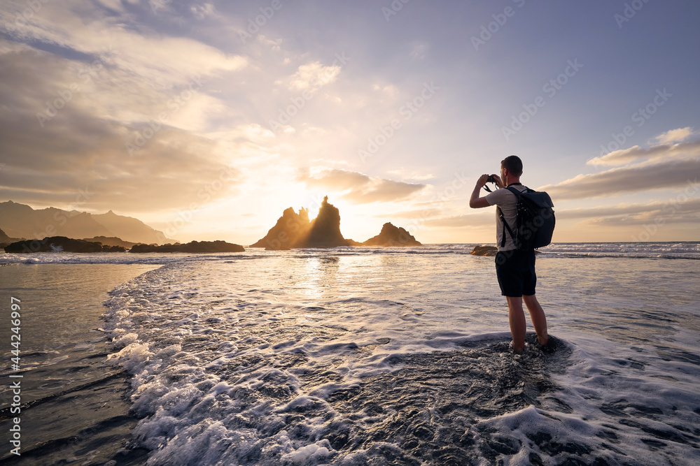 Man during photographing landscape with cliff. Young photographer on beach at beautiful sunset. Tenerife, Canary Islands, Spain. - obrazy, fototapety, plakaty 