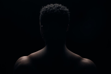 Dark portrait of a young black man.Photo from behind on a dark background