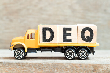 Sticker - Toy truck hold alphabet letter block in word DEQ (Abbreviation of Delivered Ex Quay) on wood background